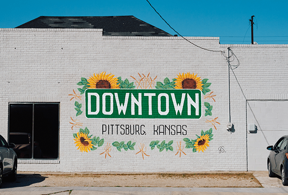 A mural reading Downtown Pittsburg, Kansas is surrounded by painted sunflowers.