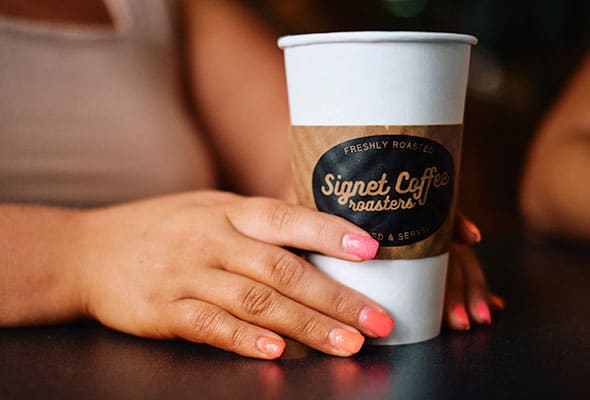 A woman holds a coffee cup with the logo of Signet Coffee.