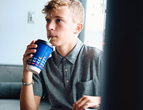 A young teenage boy sips from his coffee cup.
