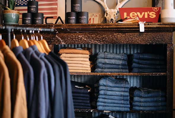 Shelves of shirts, jeans, and other men's accessories are shown in this rustic boutique.