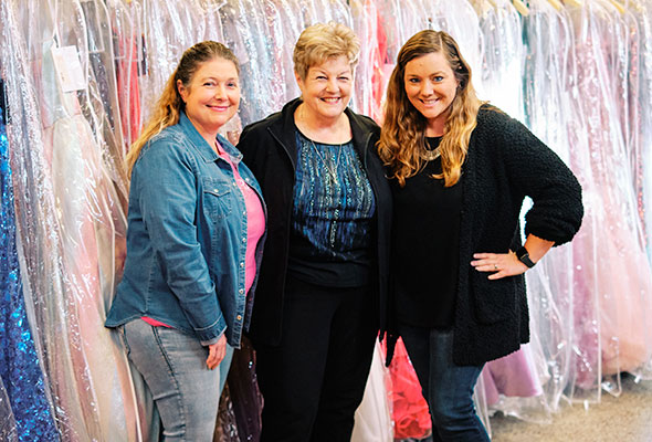 three women standing in front prom gowns